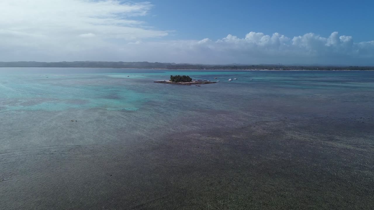 Forward glide drone shot of a small island with coconut trees in the middle of the ocean