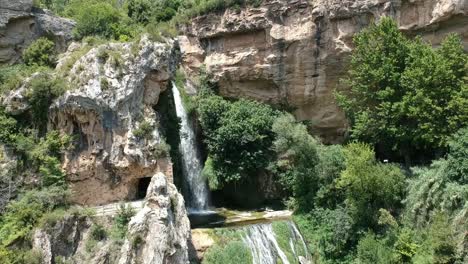 Aerial-views-of-a-waterfall-with-a-cave-and-an-old-building-in-Catalonia,-Spain