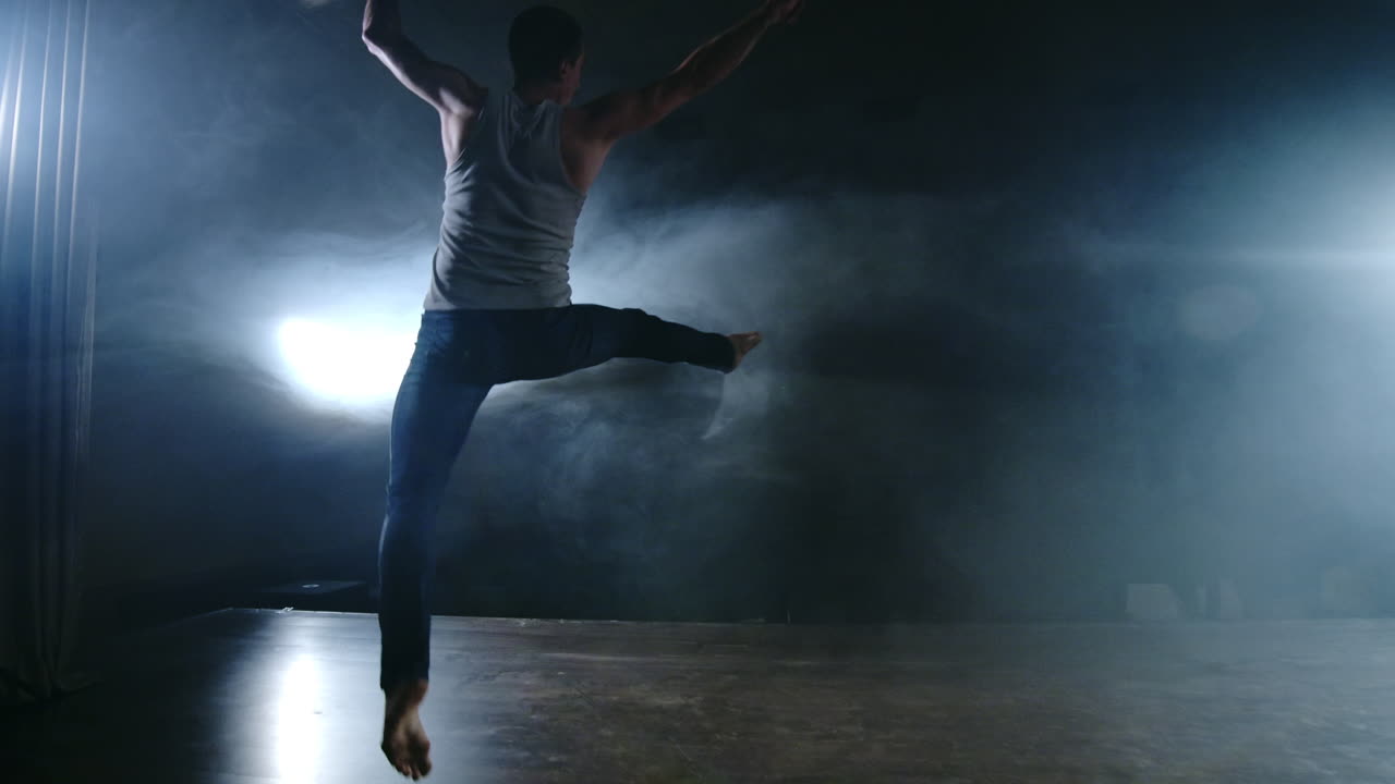 un ballet moderno un hombre realiza saltos y giros a la luz de los reflectores y el humo en un fondo oscuro. ensayo de coreografía acrobática del guión del ballet moderno.