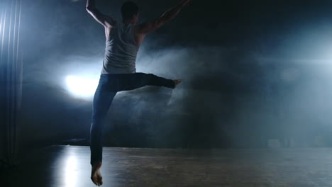 a modern ballet a man performs jumps and spins in the light of spotlights and smoke on a dark background. acrobatic choreography rehearsal of the script of modern ballet.