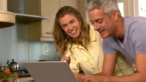 pareja feliz usando una computadora portátil en la cocina