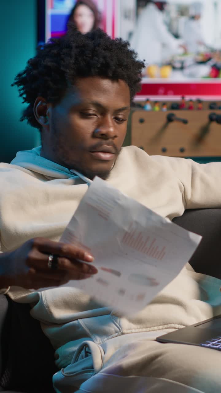 Uomo afroamericano che lavora su un portatile e rivede documenti a casa