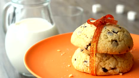 delicious sweet chocolate-chips cookies with an orange ribbon. milk-jug, on wooden table. looped