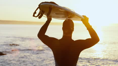 Vista-Trasera-De-Un-Surfista-Caucásico-De-Mediana-Edad-Llevando-Una-Tabla-De-Surf-En-La-Cabeza-En-La-Playa-4k