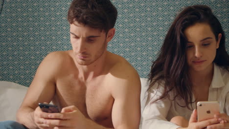 Focused-couple-scrolling-smartphones-bed.-Serious-couple-looking-phone-screens