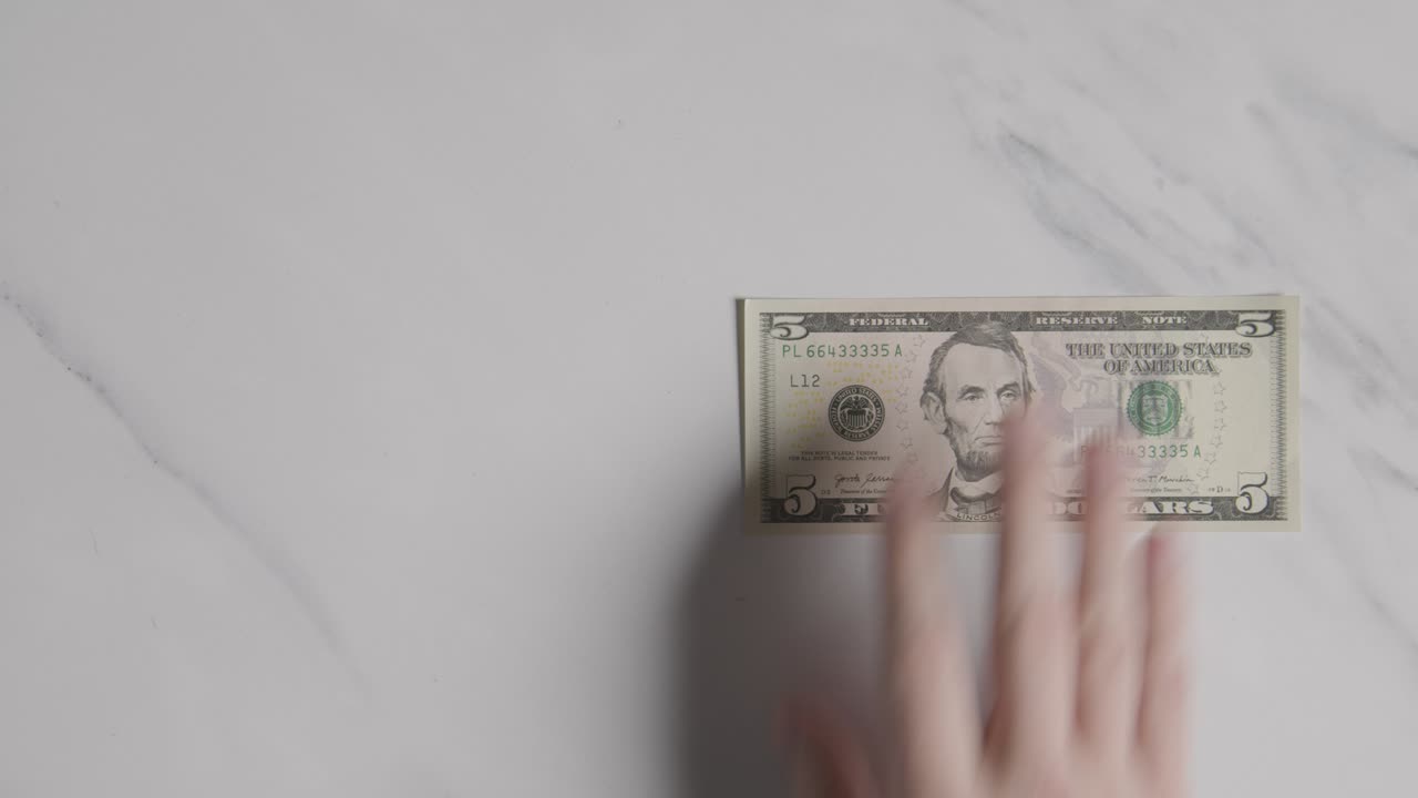 Overhead Currency Shot Of Hand Grabbing US 5 Dollar Bill On Marble Surface