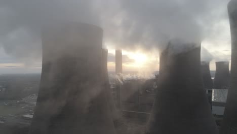 aerial slow dolly right across power station cooling towers smoke steam emissions above sunrise glow