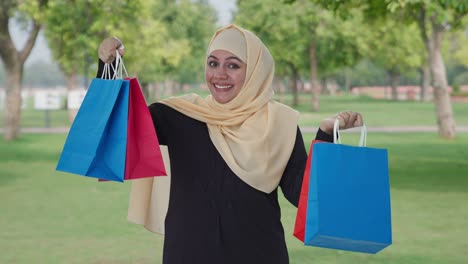 happy muslim woman posing with shopping bags in park