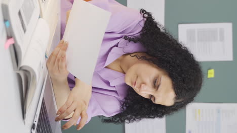 video vertical de una estudiante trabajando entre el papel y la computadora portátil.