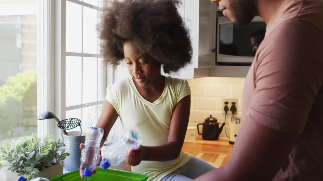 African american daughter playing with plastic bottles while sorting recycling with father in kitche