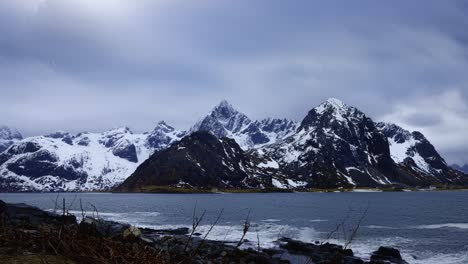 Waves-crashing-on-rocky-shore-in-a-fjord-surrounded-by-snowy-mountains