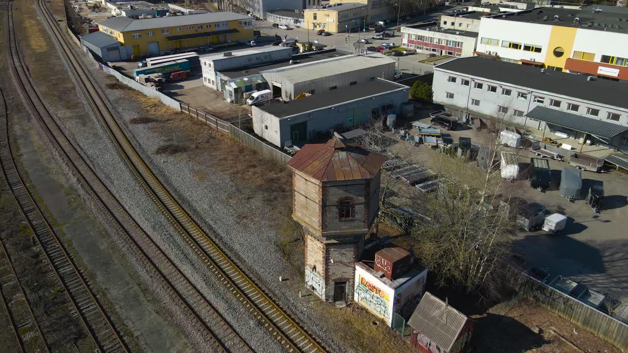 Aerial drone footage ascending and revealing a old retro train constructor worker tower made out of bricks, that is standing by traintracks or a railroad station on a warm sunny day in Tallinn Väike.