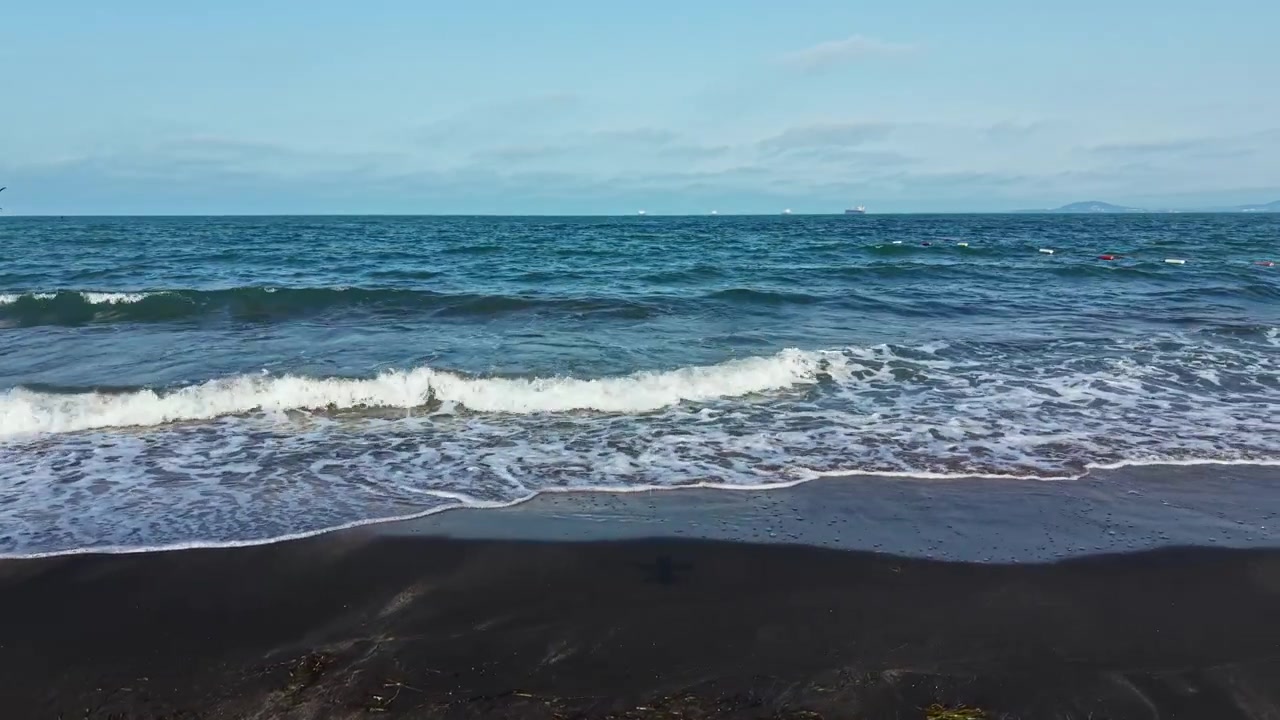 Le onde si infrangono sulla riva mentre si praticano sport acquatici in una giornata di sole in spiaggia, con cieli sereni e acque calme.