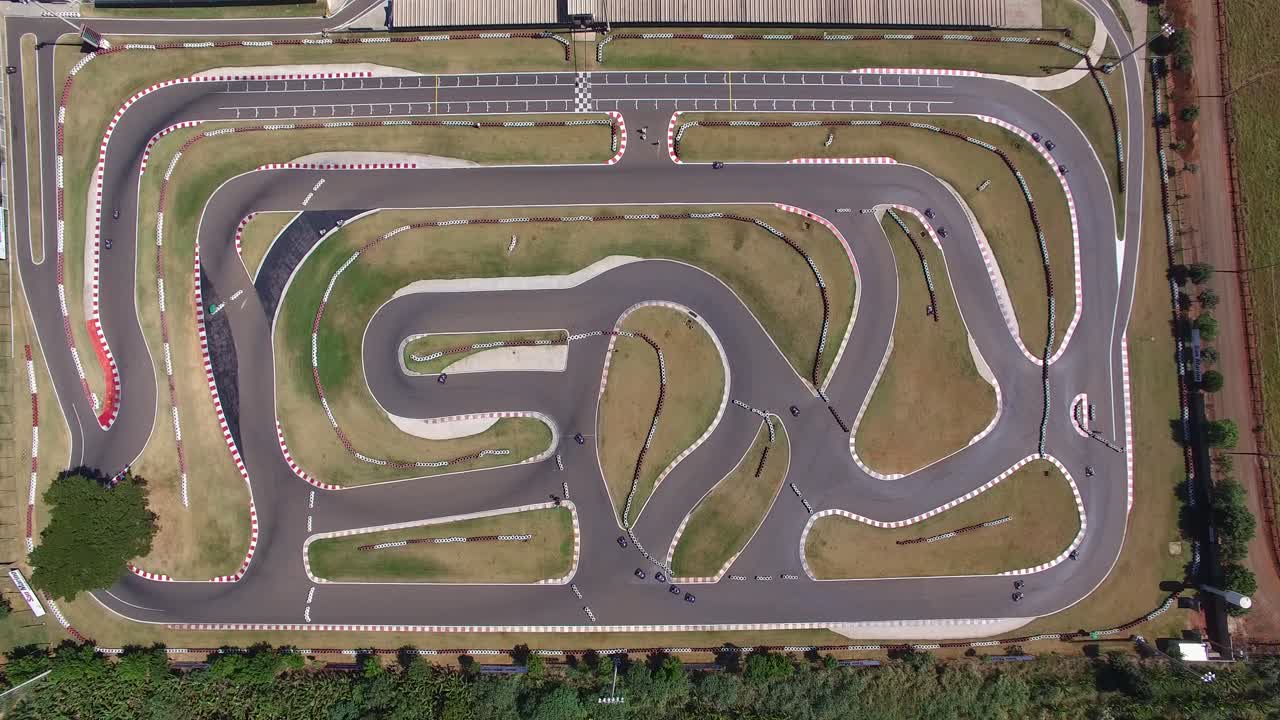 Aerial birdseye static shot of kart track on sunny day, drivers racing