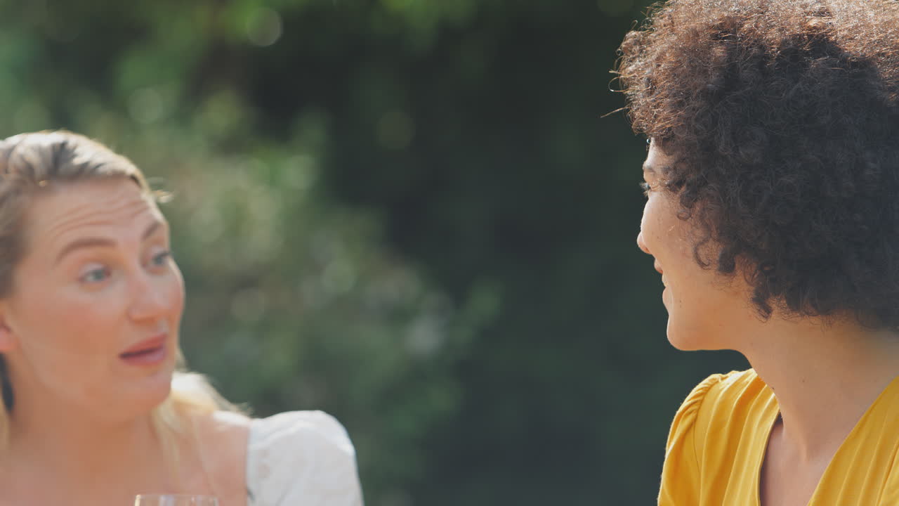 tres amigas sentadas al aire libre en el jardín de verano en casa bebiendo vino