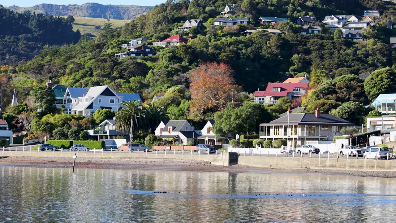 A serene coastal town with colorful houses and lush greenery, captured in bright daylight with calm waters reflecting the scenery