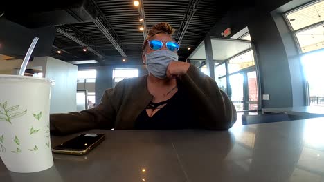 black woman with mask on sitting at restaurant waiting on to go order wearing protective face mask and sunglasses