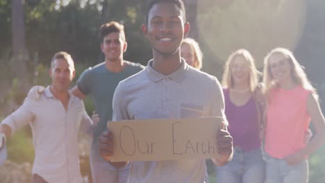 mid adults smiling and looking at camera with man holding our earth sign during river clean-up day