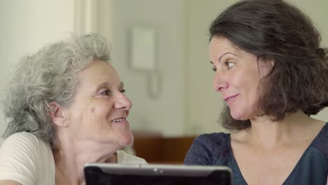 smiling mature daughter and mother using tablet.