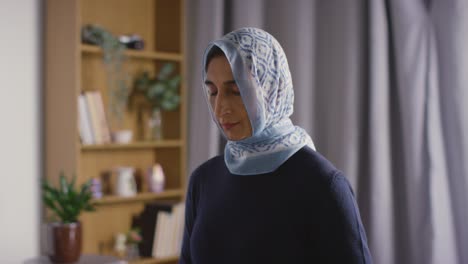 mujer musulmana con hijab rezando sosteniendo cuentas de oración en casa