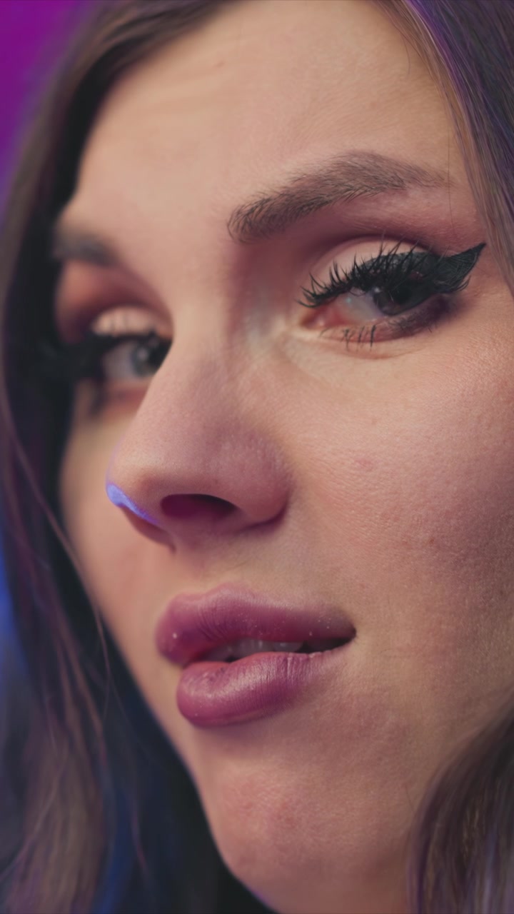 Close up view of woman face focusing on her nose and lips with subtle movements. Soft purple lighting creates moody ambiance highlighting skin texture details. Background remains out