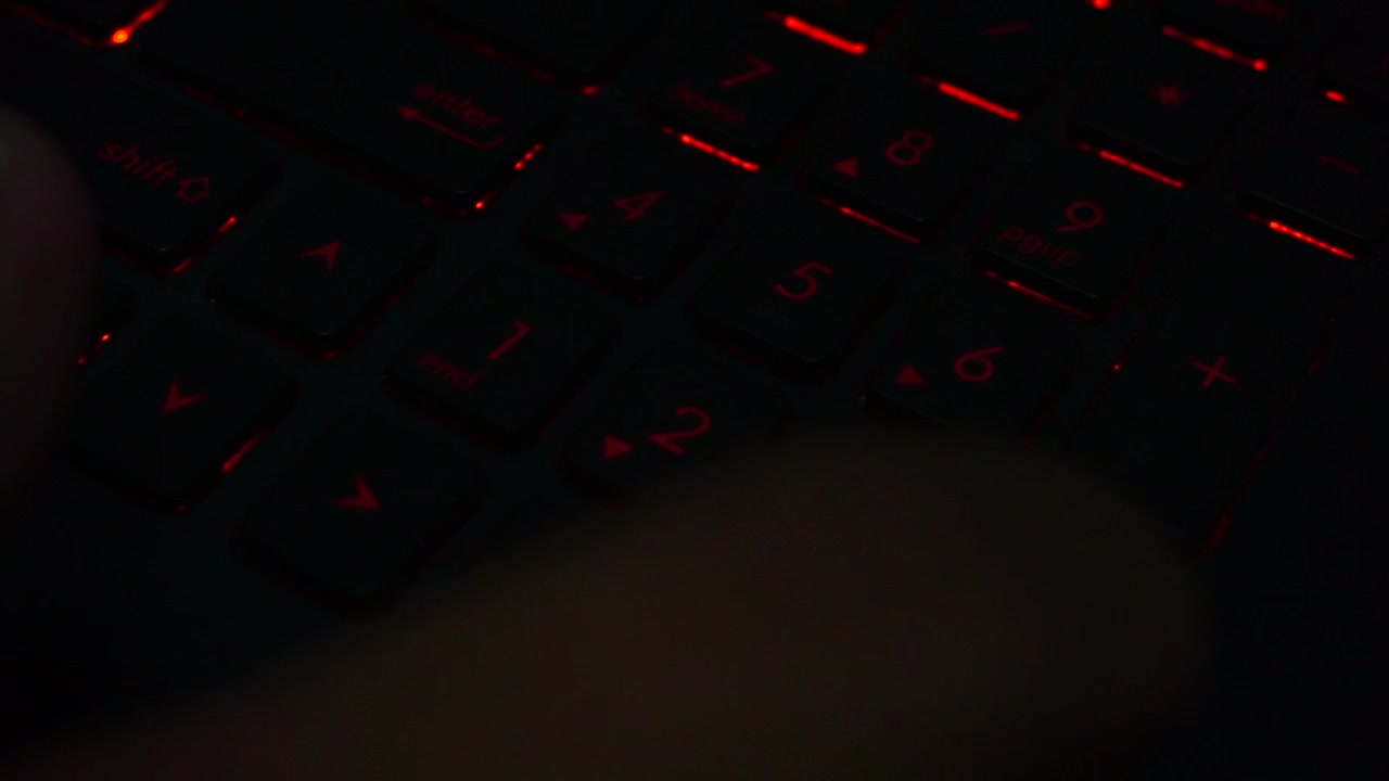 Top view of hand typing on red lighting keyboard number of laptop in dark room,close up