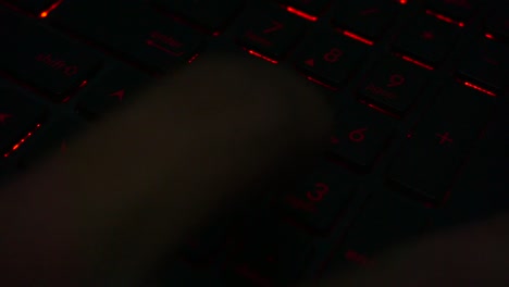 Blick-Von-Oben-Auf-Die-Hand,-Die-Auf-Der-Tastatur-Mit-Roter-Beleuchtung-Die-Nummer-Des-Laptops-In-Einem-Dunklen-Raum-Eingibt,-Nahaufnahme