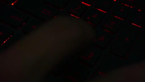 top view of hand typing on red lighting keyboard number of laptop in dark room,close up