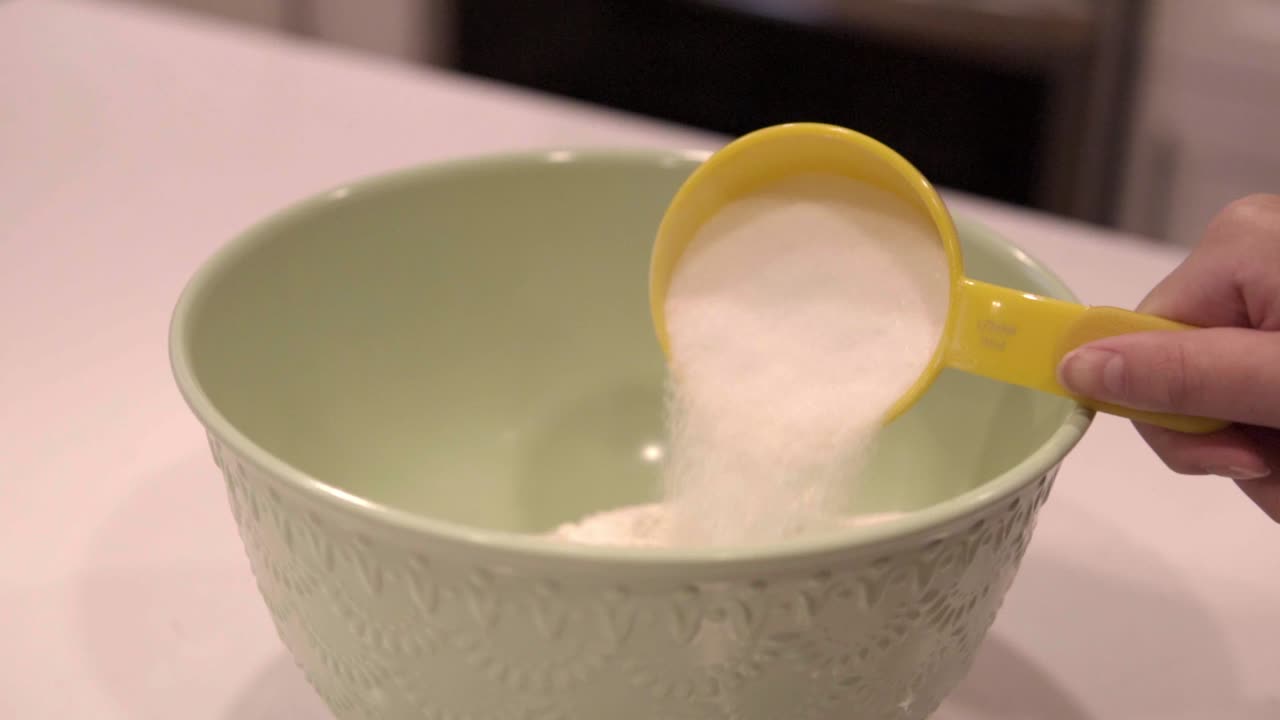 Slow motion of sugar pouring from a measuring cup into a large bowl