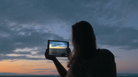 mujer con pad haciendo fotos del mar y el cielo en el anochecer