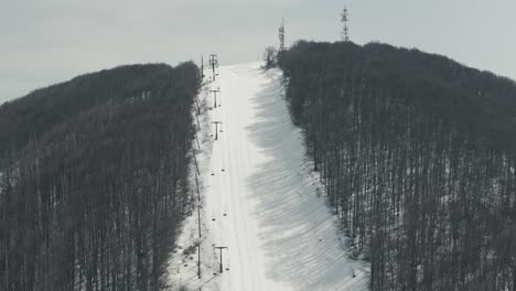 A-drone-shot-of-forest-mountains-with-snow,-warm-weather,-flying-above-the-snowboard-hill,-4K-video,-European-winter-nature