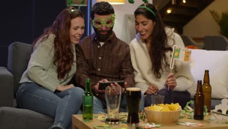 grupo de amigos disfrazándose en casa o en un bar celebrando en la fiesta del día de san patricio mirando fotos en el teléfono 2