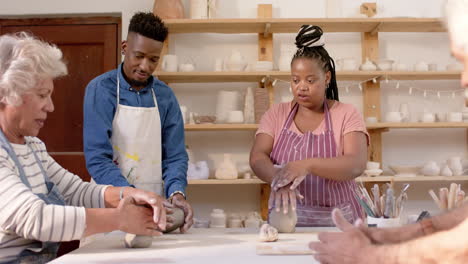 happy diverse group of potters shaping clay with hands and discussing in pottery studio