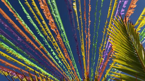 multicoloured ribbons decorating the street in front of the blue sky and palm leaves.