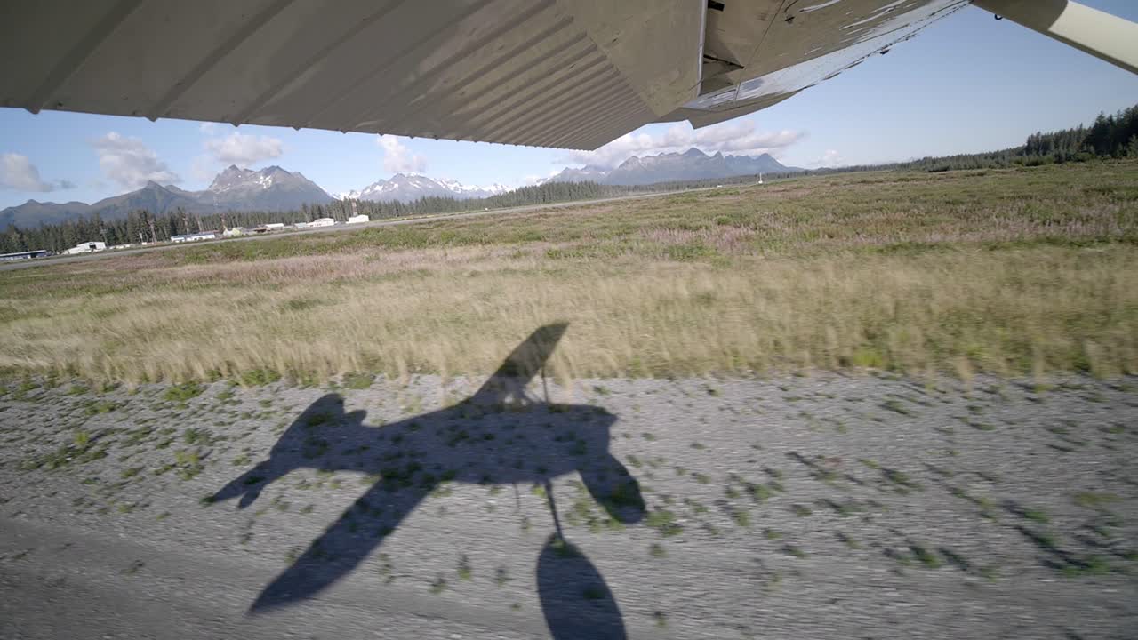 Passasjerperspektiv av vinge og skygge på et lite sivilt fly som tar av fra rullebanen på en flyplass i Alaska, USA.
