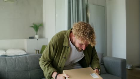 hombre emocionado desembozando un paquete en un sofá