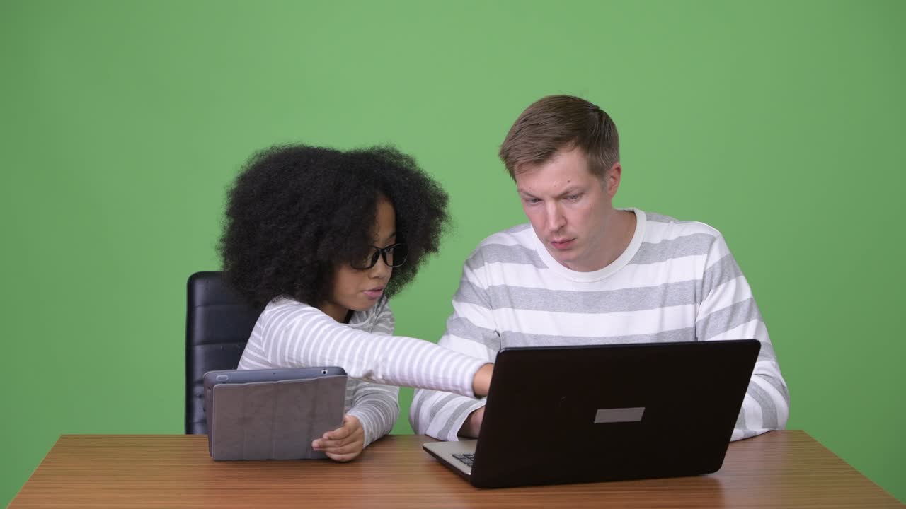 Young African girl and young Scandinavian man using gadgets together