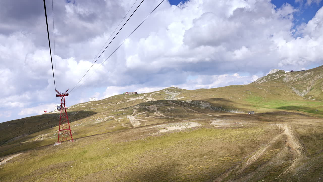 Cable car ride over mountain landscape. A cable car glides above lush green hills with distant peaks under a partly cloudy sky during the day