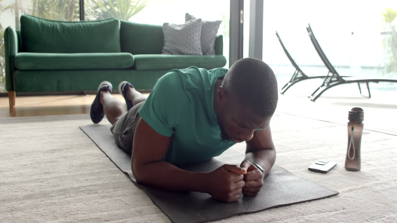 Strong and fit African American man doing plank exercise on yoga mat at home