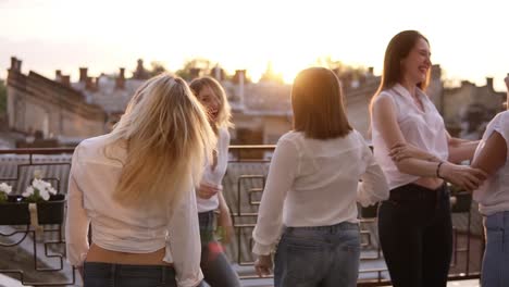 six women are hanging out together on the terrace. all in the same style clothes. dancing and jumping. casual clothes. cityscape background. hen party concept. dusk. slow motion