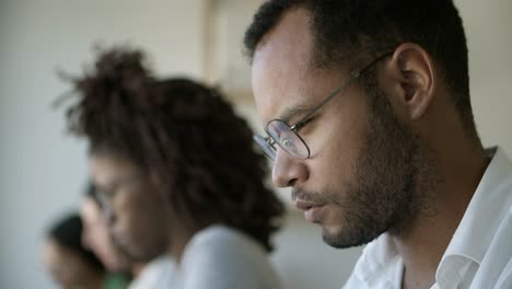 side view of thoughtful man in eyeglasses typing on laptop