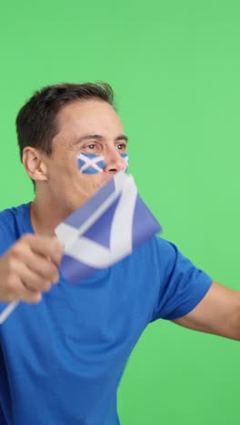 Man cheering for Scotland waving a national flag looking away