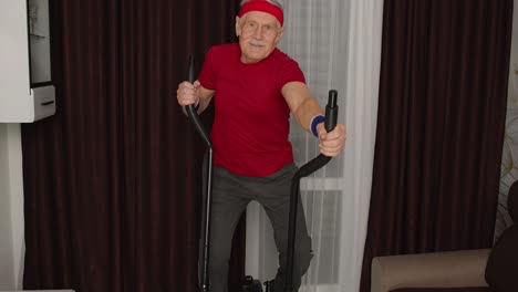 hombre adulto anciano sano y activo en ropa deportiva usando orbitrek, entrenamiento de cardio en casa