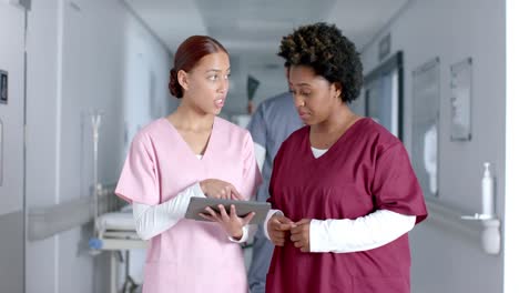 diverse female doctors discussing work and using tablet in corridor, slow motion