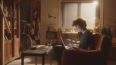 young man with headphones using laptop in cozy, warmly lit apartment