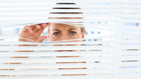 una mujer de negocios severa mirando a través de las persianas.