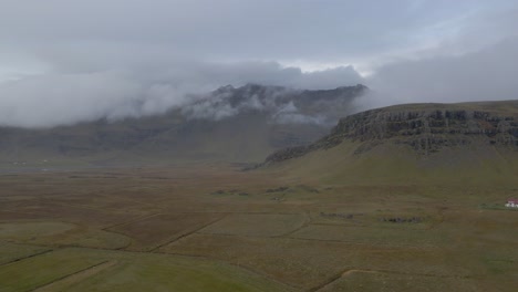 Grüne-Und-Flache-Isländische-Landschaft-Mit-Bergen,-Die-Von-Niedrigen-Wolken-Umhüllt-Sind,-Island