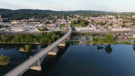 aerial turning pan of columbia, pennsylvania with smooth blue water of susquehanna river, following boat leaving wake, clear summer evening