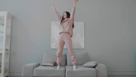 funny young caucasian woman with glasses happily dancing and jumping on sofa.