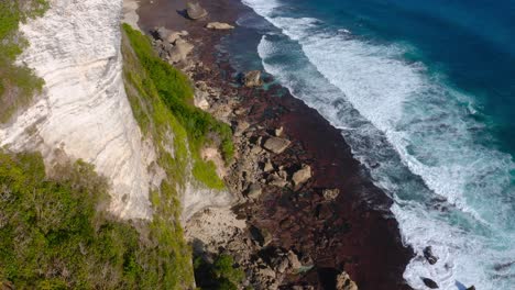 aerial tilt down of the rocky beach next to epic karong boma cliff
